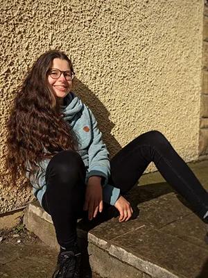 Photo of Alex sitting outdoor, in the sun, on a step in front of a wall
