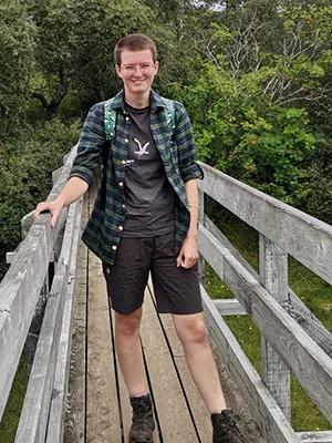 Photo of Rhoslyn standing on a bridge in front of a woodland landscape