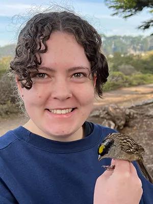 Photo of Caroline outdoors holding a small bird with a black and yellow-striped head