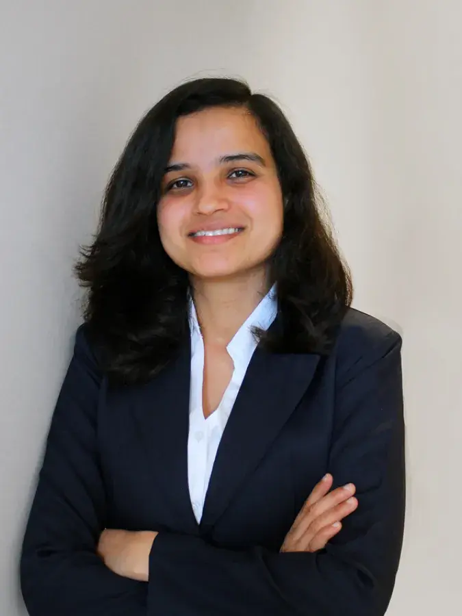 A woman in a smart jacket and shirt with her arms folded. She has shoulder length dark hair and is smiling.