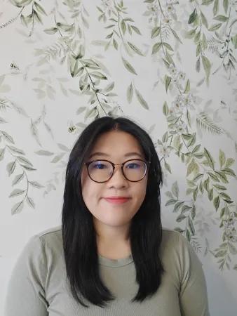 A person smiling in front of a floral wallpaper