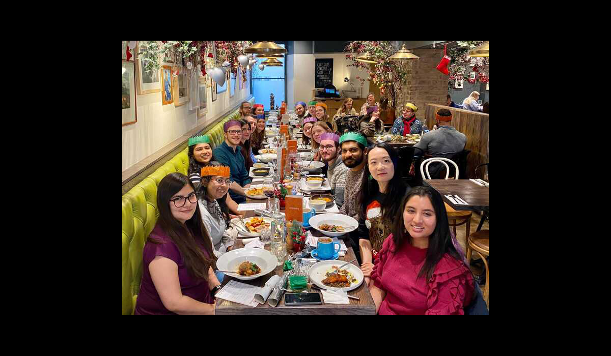 Photo of the lab group sitting round a table in a restaurant with plates of food, some wearing paper crowns