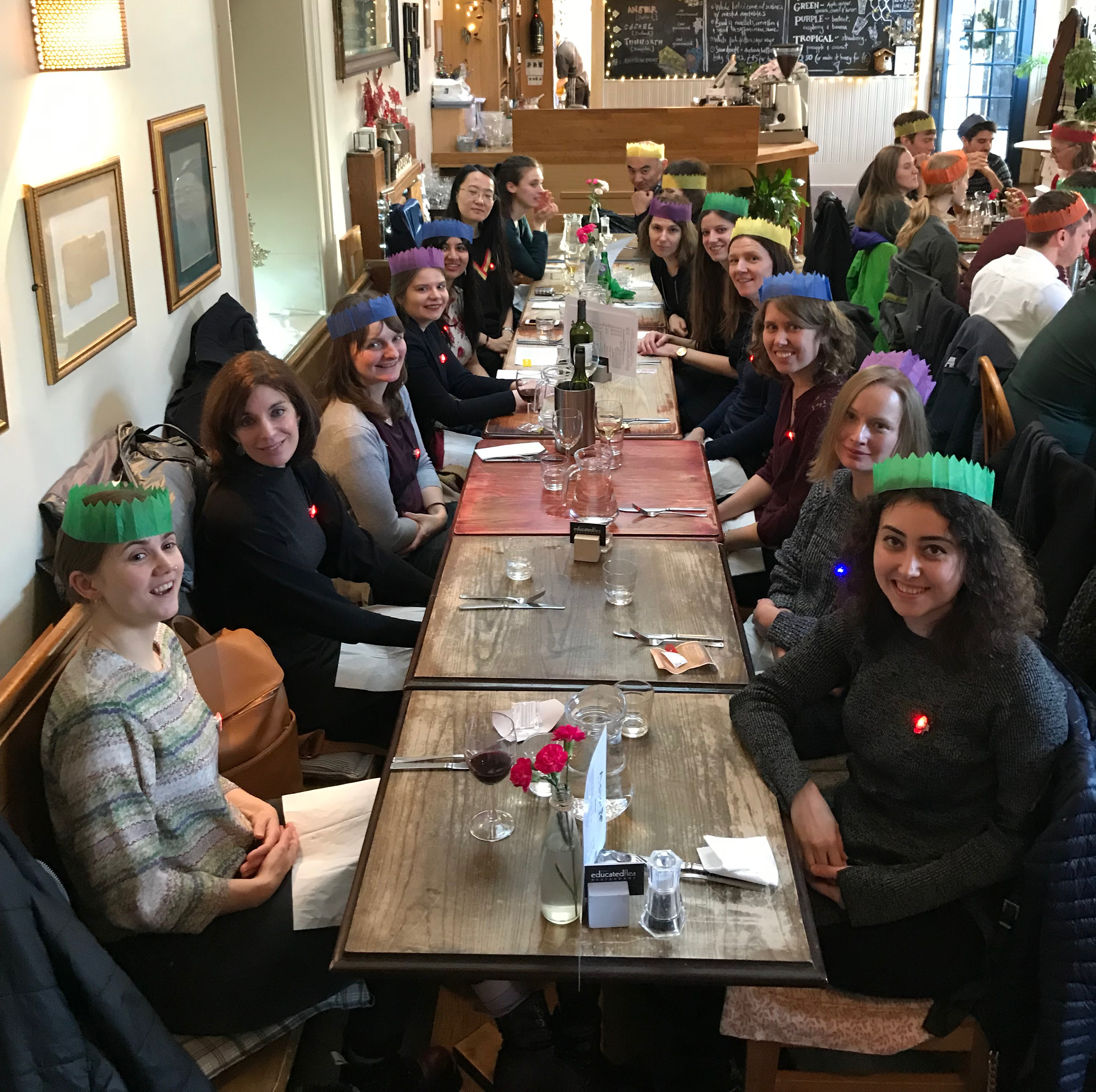 Photo of the lab group sitting round a table in a restaurant, some wearing paper crowns