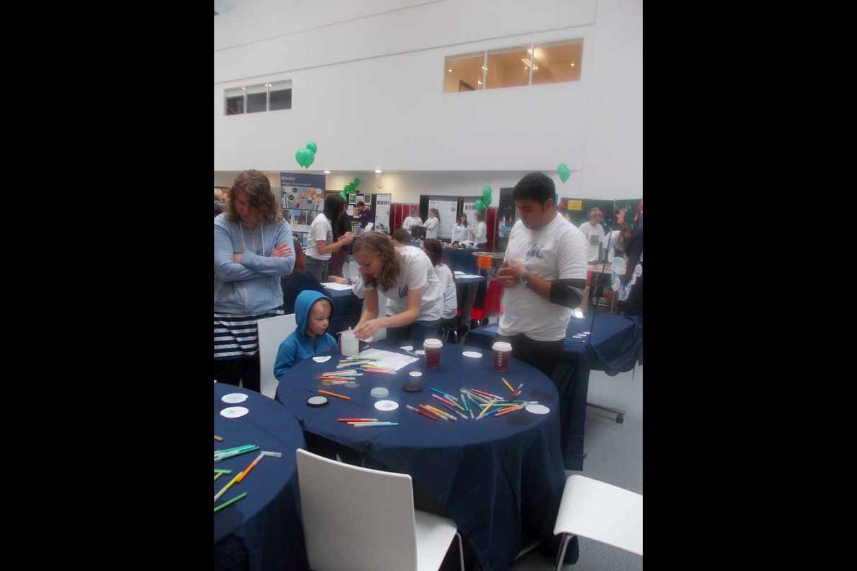 Photo of lab group members at the Midlothian Science Festival, with a child using paper and coloured pencils