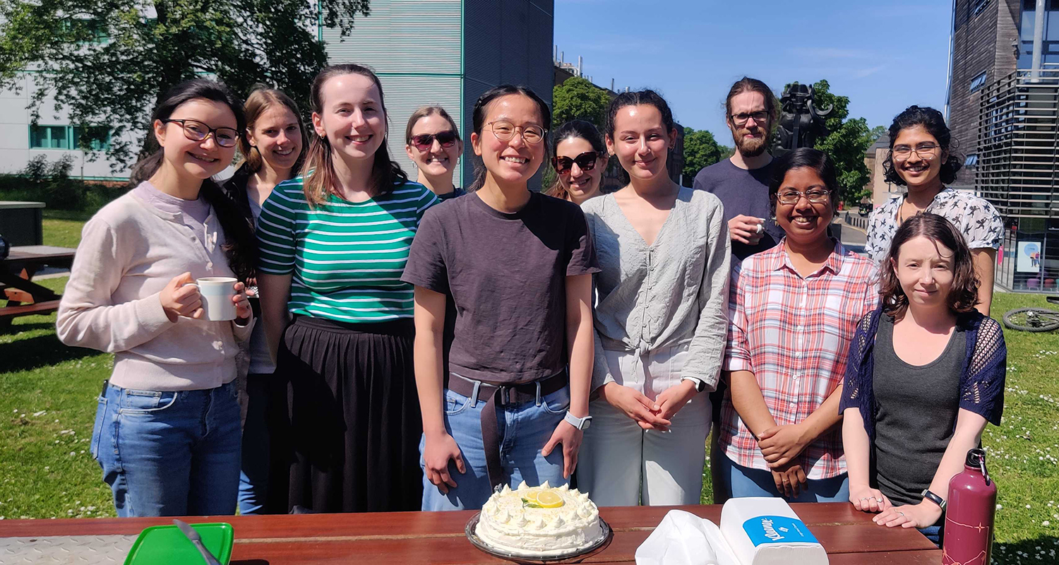 Photo of lab group members standing outside in front of a tablw with a birthday cake on it