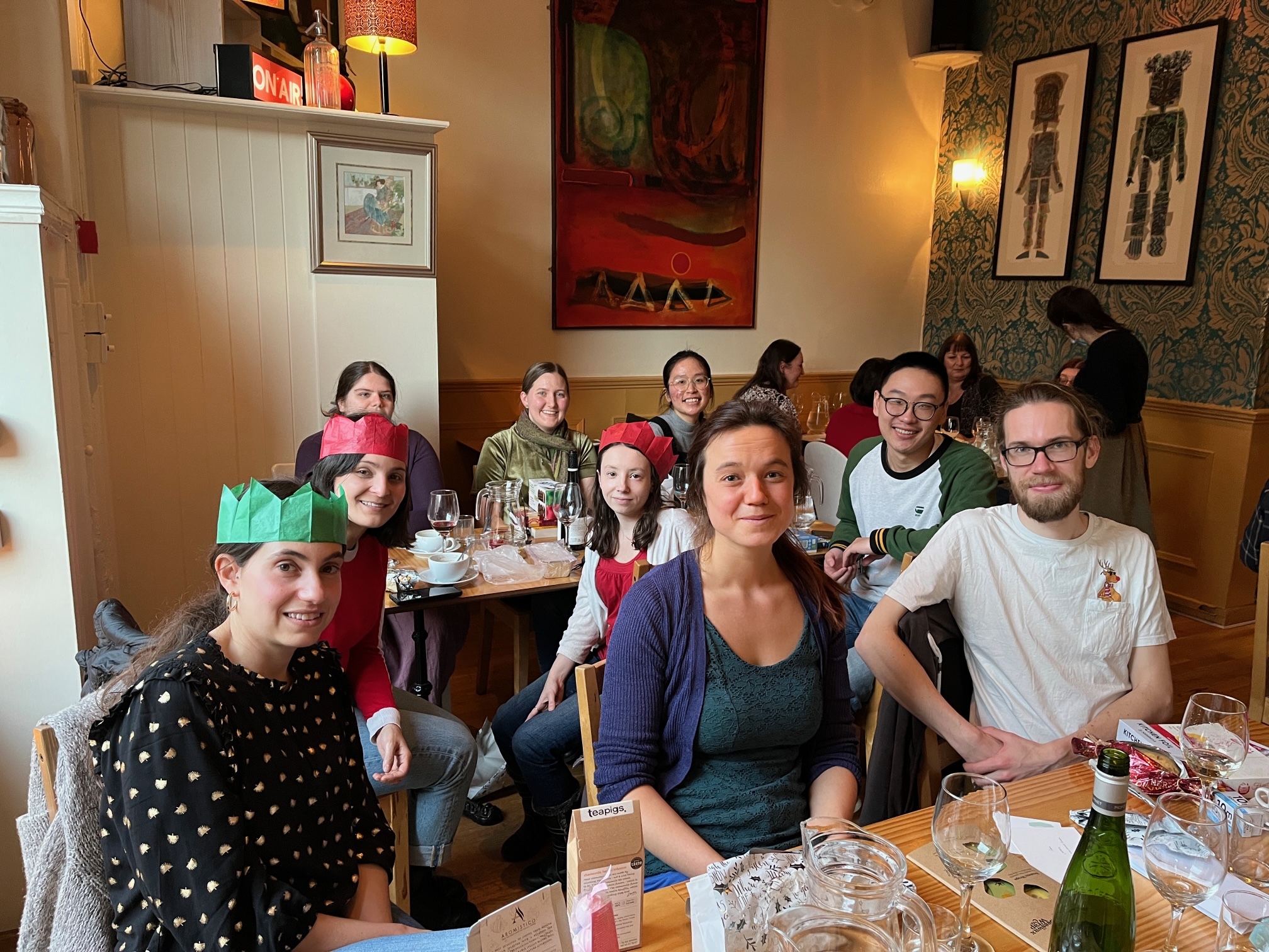 Group photo with the lab members seated at tables in a restaurant, some wearing paper crowns