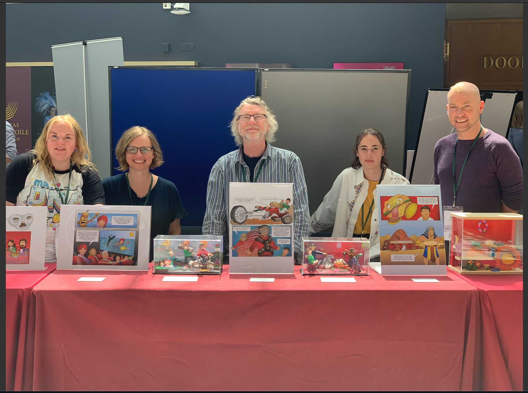 Photo of researchers sitting at table at the exhibition, displaying illustrations and figures in glass cases from the comics