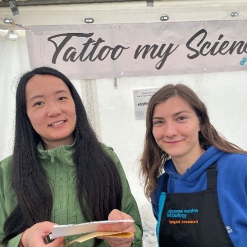 A scientist and member of the public pose for a photo in front of the festival stall